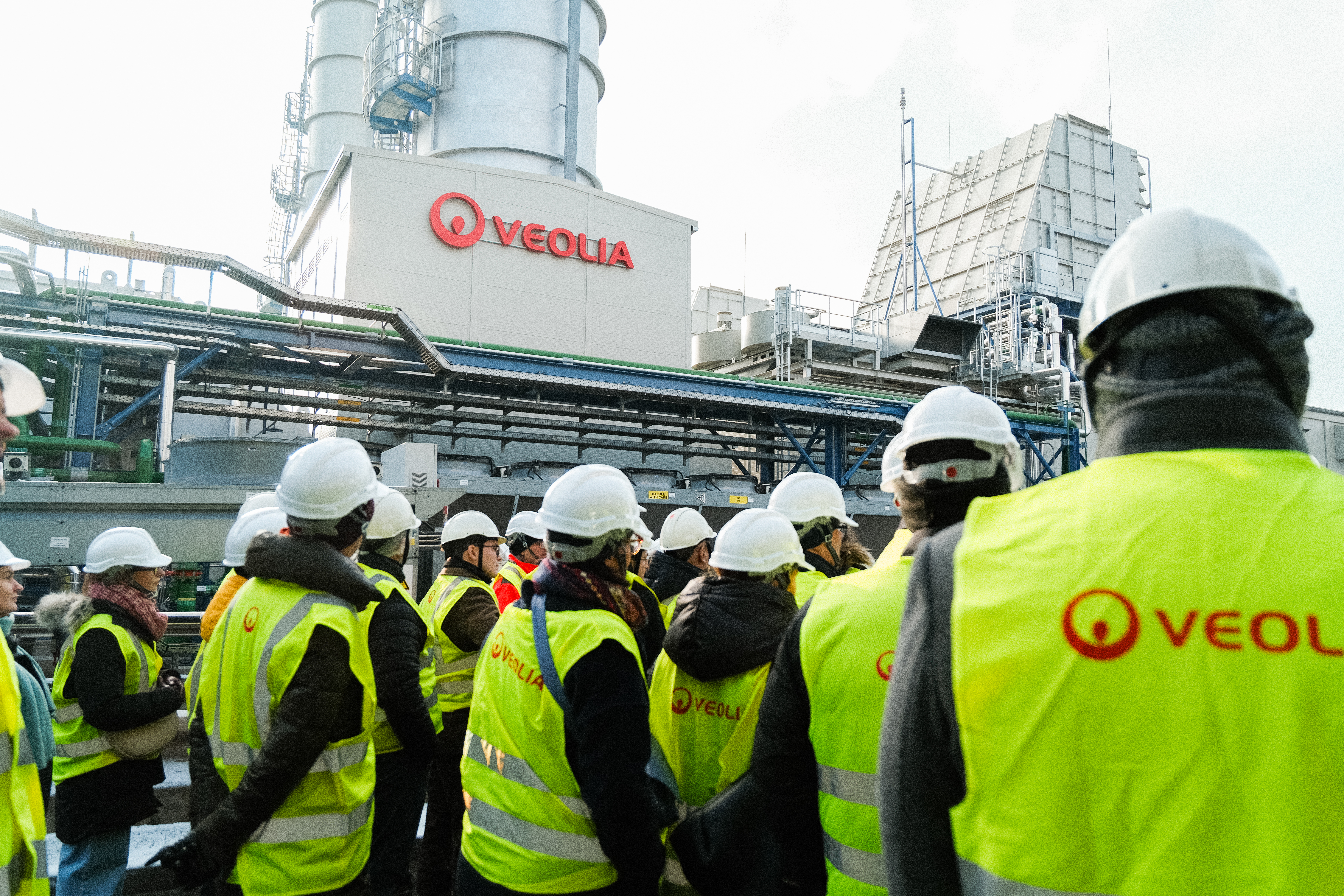 Zdjęcie przedstawia kilka budynków Veolii, stojących obok siebie w tle oraz ludzi na pierwszym plani