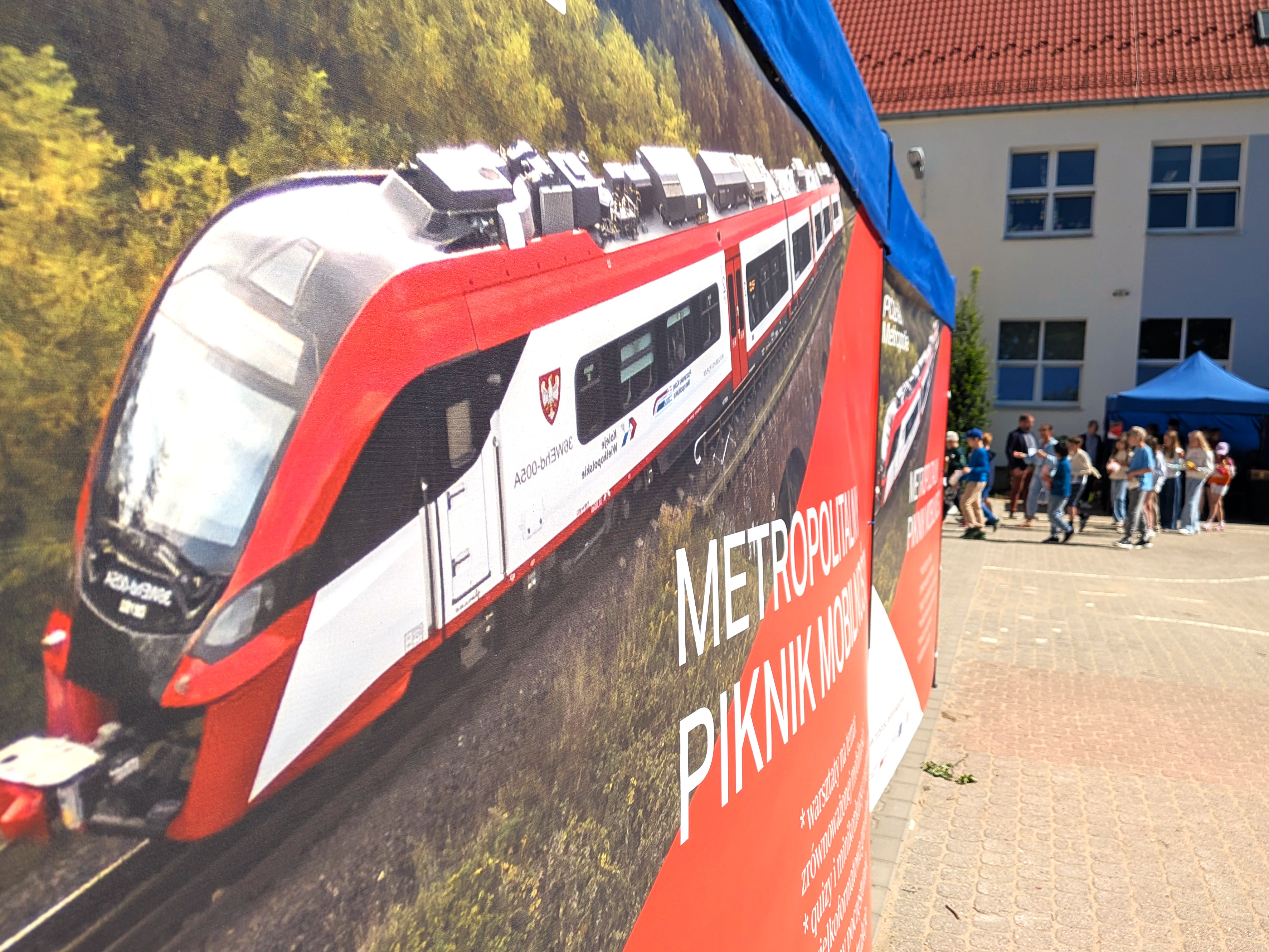 Baner z widokiem pociągu i napisem METROPOLITALNY PIKNIK MOBILNOŚCI, w tle grupa młodzieży i namiot.