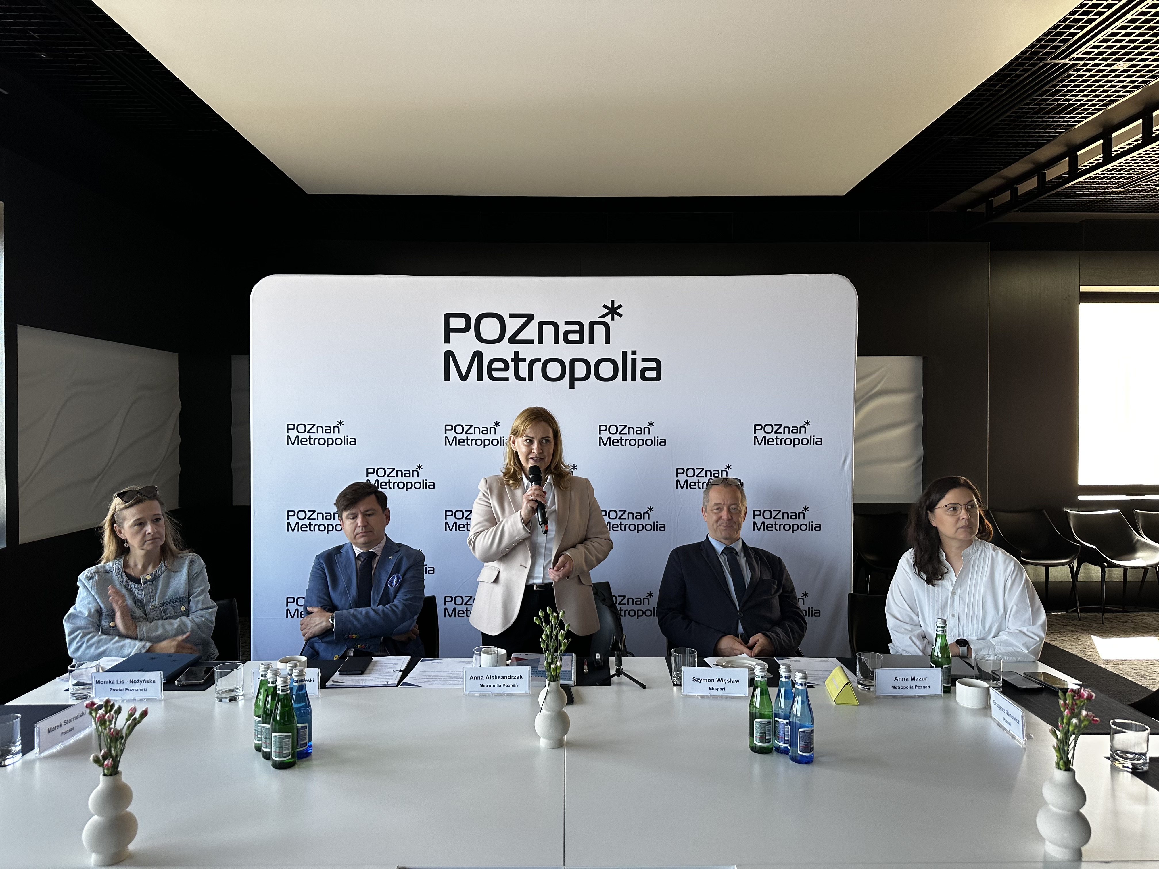Zdjęcie przedstawia kobietę przemawiającą z mikrofonem w ręce (dyrektorka Metropolii Poznań), obok n