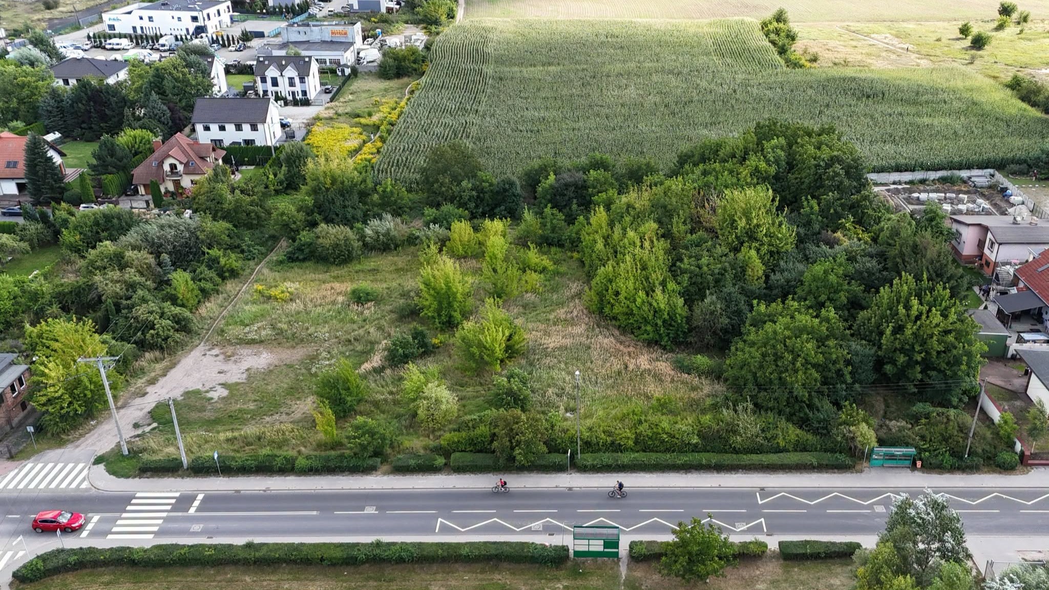 Fotografia z drona przedstawiająca niezagospodarowany teren zielony, na pierwszym tle asfaltowa ulic