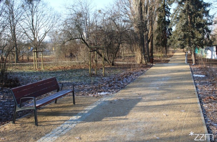 Fotografia przedstawia skwer z alejką i ławką.