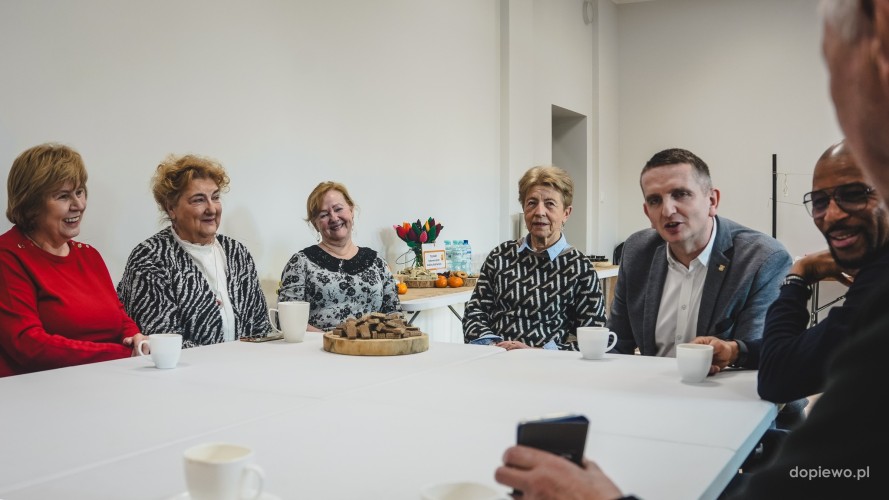 Zdjęcie przedstawia grupę seniorów i Wójta Gminy Dopiewo - siedziących przy stole w pomieszczeniu.