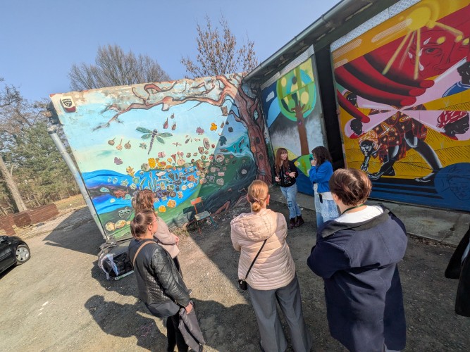 Widok grupy osób stojących przed garażami ozdobionymi kolorowymi malowidłami