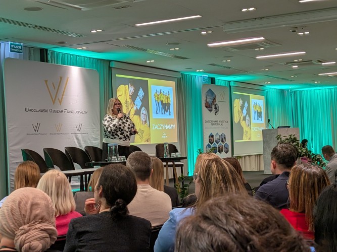 Widok sali konferencyjnej z grupą osób siedzących i zwróconych w kierunku sceny