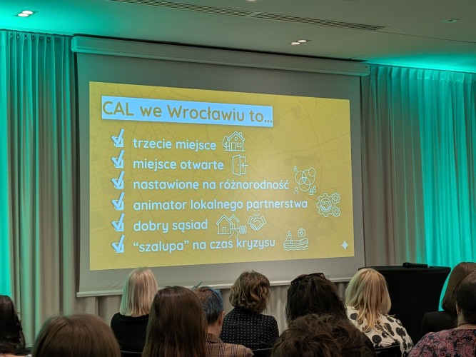 Widok sali konferencyjnej z grupą osób siedzących i zwróconych w kierunku sceny