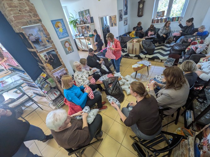 Widok sali warsztatowej z grupą osób wykonujących prace plastyczne