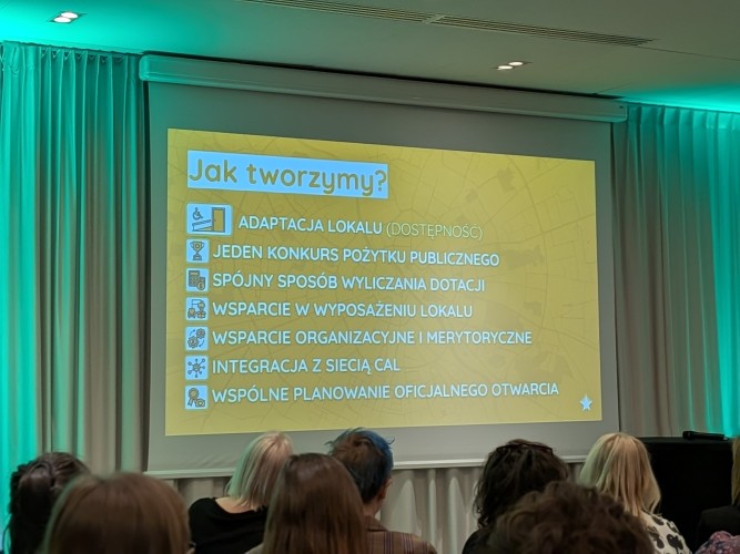 Widok sali konferencyjnej z grupą osób siedzących i zwróconych w kierunku sceny