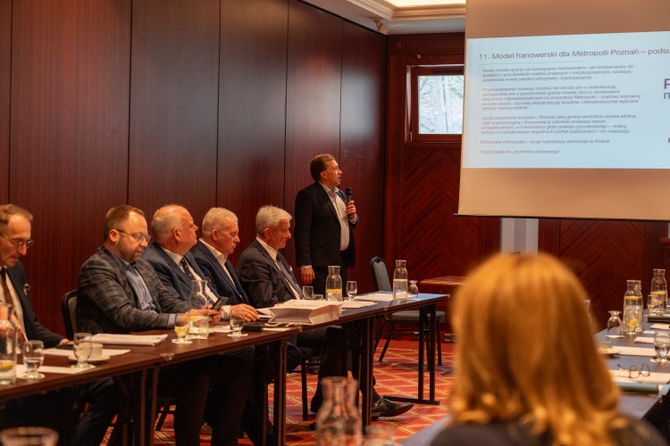 Zdjęcie przedstawia prezentującego mężczyznę, a obok niego siedzących ludzi.