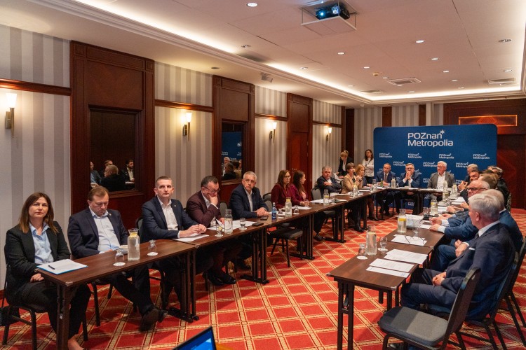 Zdjęcie przedstawia widok sali oraz stół, przy którym zasiadają osoby.