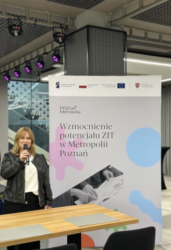 Zdjęcie przedstawia przemawiającą kobietę (Dyrektorkę Metropolii Poznań), obok niej widoczna jest ścianka z napisem oraz logotypami projektu.