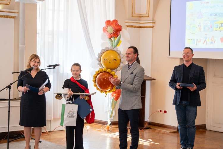 Zdjęcie przedstawia dziewczynkę, której wręczane są nagrody przez burmistrza Szamotuł.