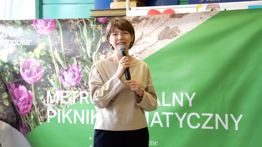 Kobieta z mikrofonem na tle baneru z zapisem METROPOLITALNY PIKNIK KLIMATYCZNY