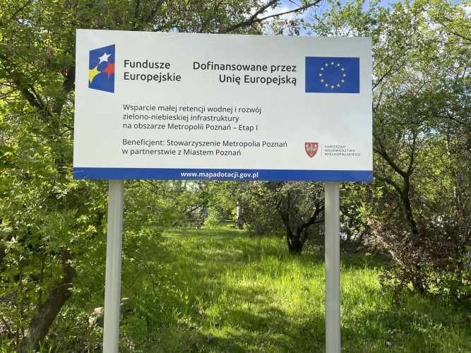 Zdjęcie przedstawia widok ze skweru przy ul. Wiatracznej. Na pierwszym planie tablica informacyjna.