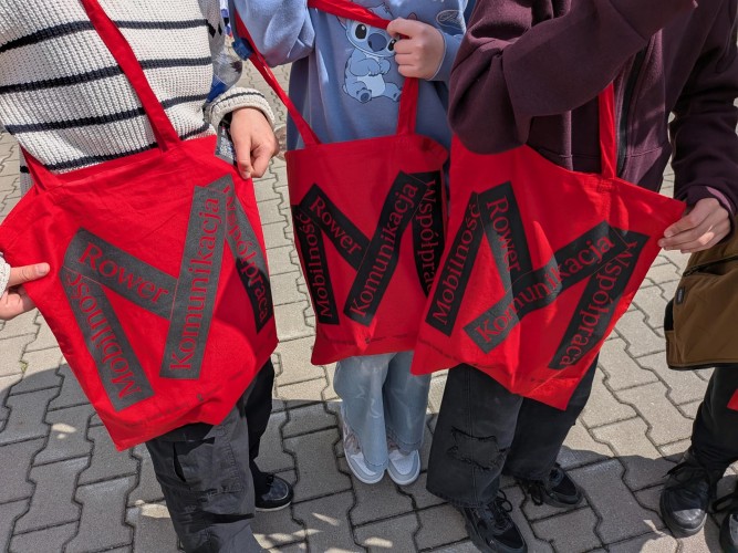 Zdjęcie przedstawia czerwone torby z logiem Metropolii Poznań oraz hasłami.