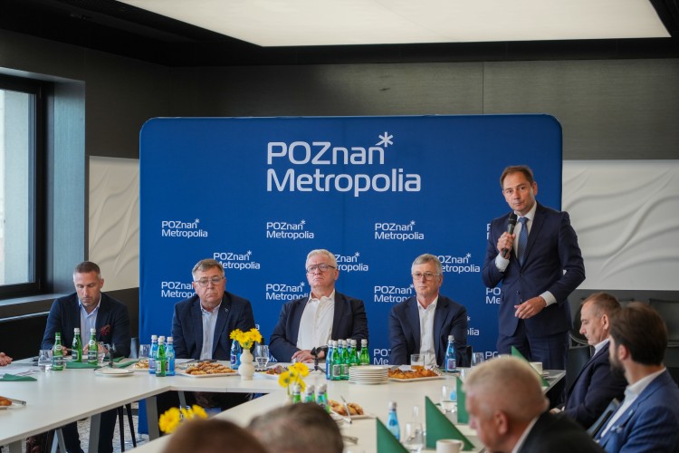 Zdjęcie przedstawia kilku włodarzy siedzących przy stole oraz przemawiającego mężczyznę z mikrofonem w ręce (wójt Rokietnicy, przyszły Zastępca Prezydenta Miasta Poznania).