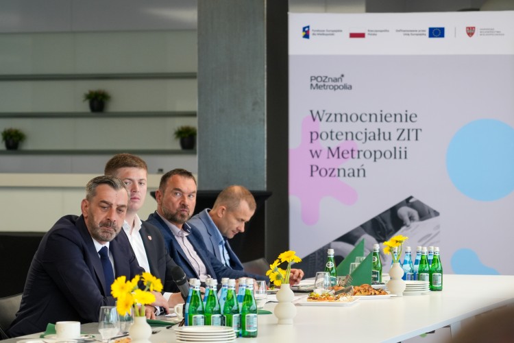 Zdjęcie przedstawia kilku mężczyzn siedzących obok siebie (włodarze gmin i miast Metropolii Poznań).