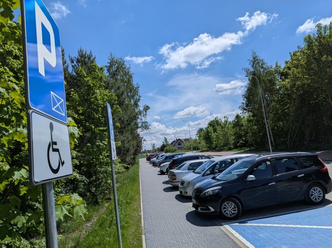 Zdjęcie przedstawiające znaki pionowe informujące o miejscach dla niepełnosprawnych na parkingu samochodowym.
