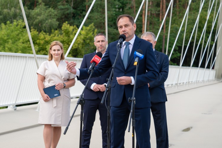 Cztery osoby stoją na kładce pieszo-rowerowej. Mężczyzna stoi przed trzema mikrofonami.