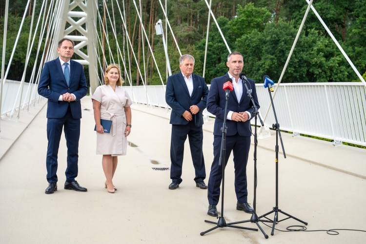 Cztery osoby stoją na kładce pieszo-rowerowej. Mężczyzna stoi przed trzema mikrofonami.