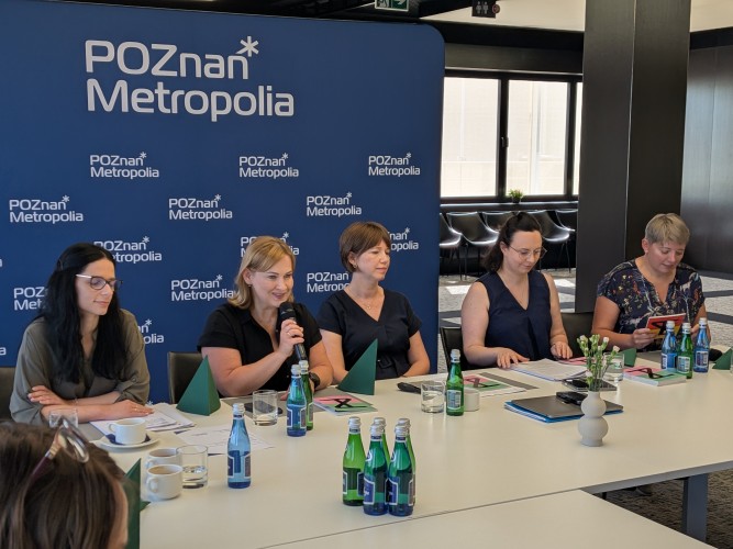 Zdjęcie przedstawia kilka kobiet siedzących przed ścianką.
