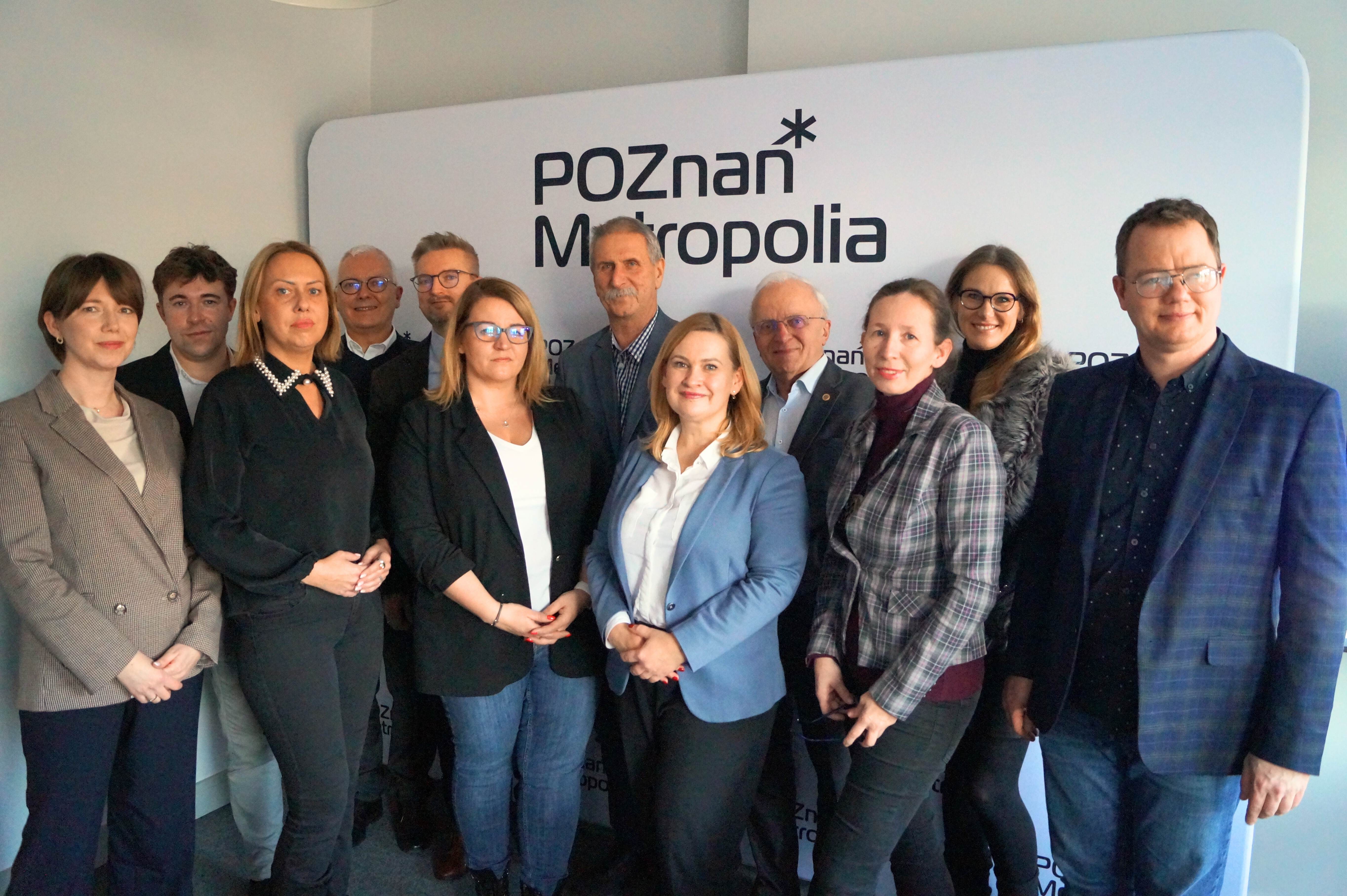 Zdjęcie przedstawia grupę pozujących na tle ścianki zdjęciowej.